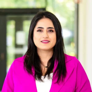 Ein Portraitfoto zeigt eine junge Frau mit schwarzen Haaren und einem pinken Blazer.